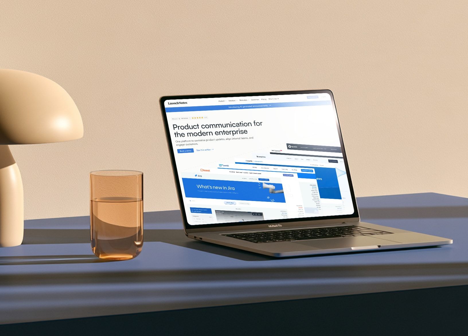 The live LaunchNotes homepage on a laptop on a blue desk, with the headline “Product communication for the modern enterprise” above a fanned stack of customer update pages from Jira, Toast, Cvent, LangChain, and SpotOn.